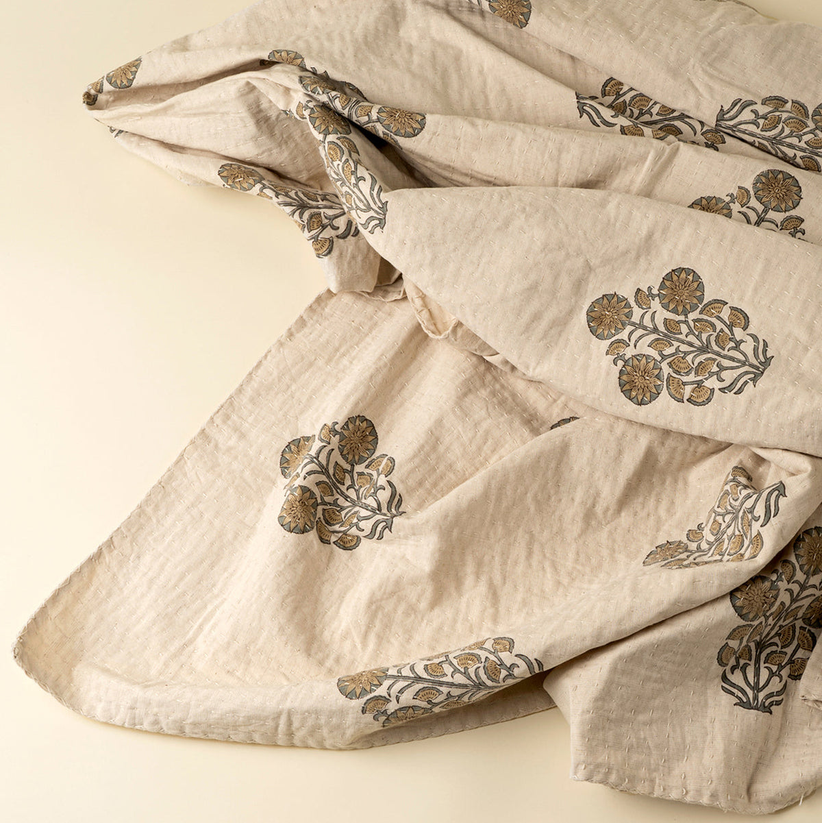Couverture Kantha beige drapée, motifs floraux ocre sur tissu matelassé