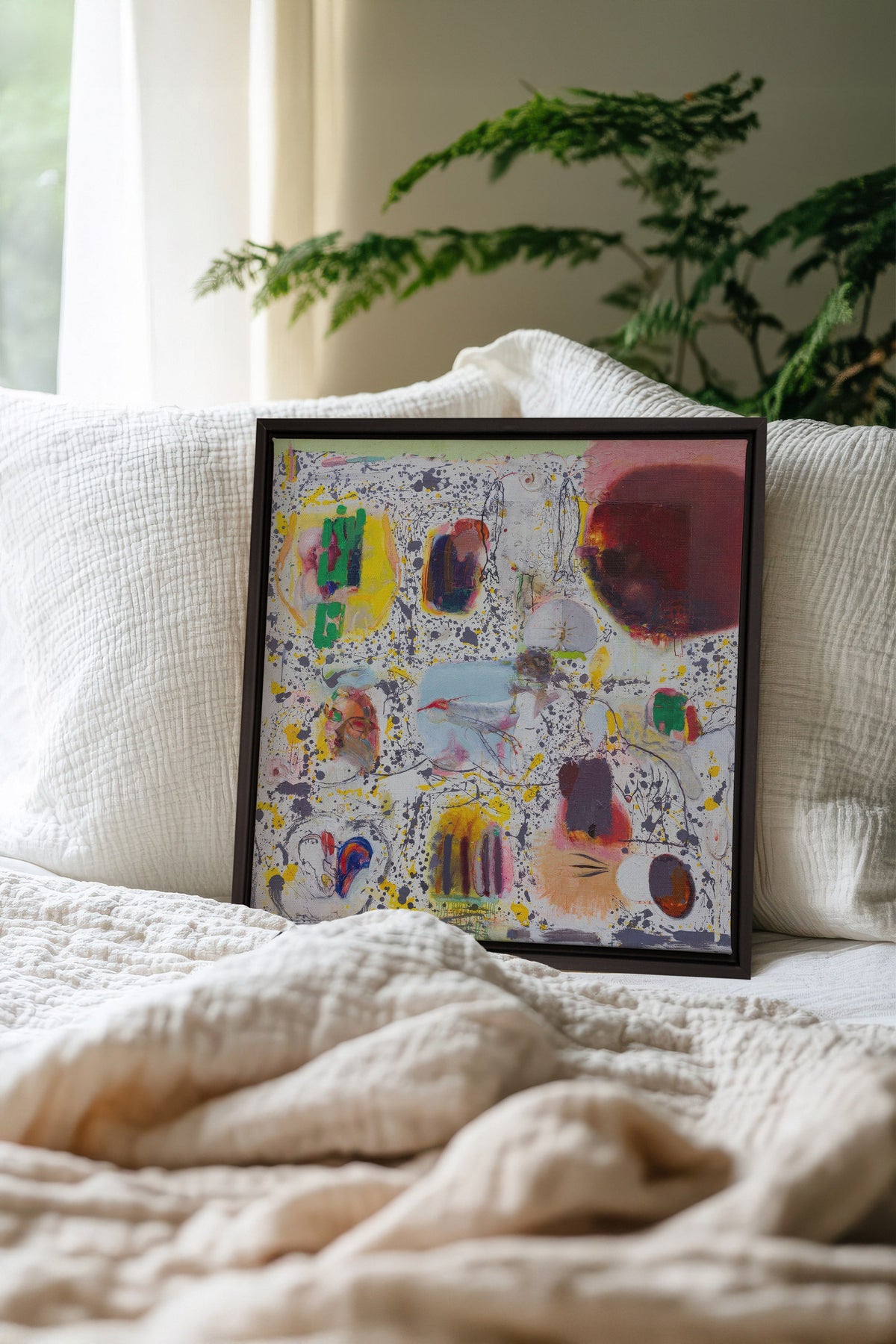 Œuvre sur toile étirée abstraite avec cadre noir, couleurs vives sur un lit.
