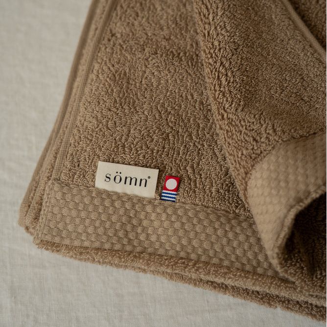 Grande serviette de bain en coton Asobi beige repliée avec étiquette sömn