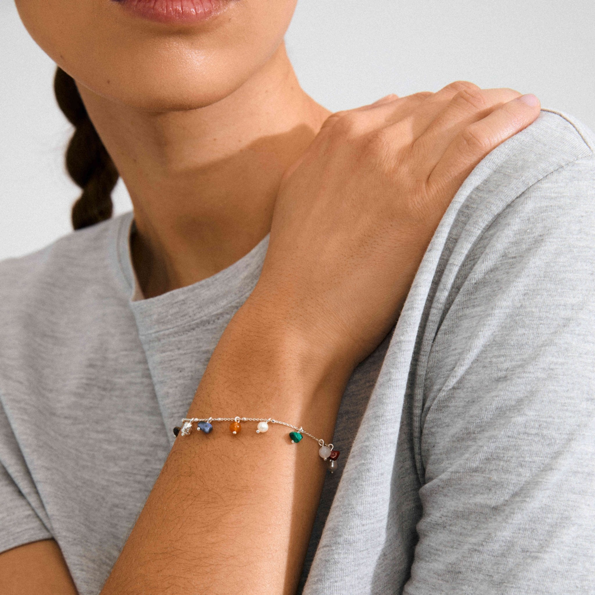 Bracelet fin doré à petites pierres multicolores, porté au poignet