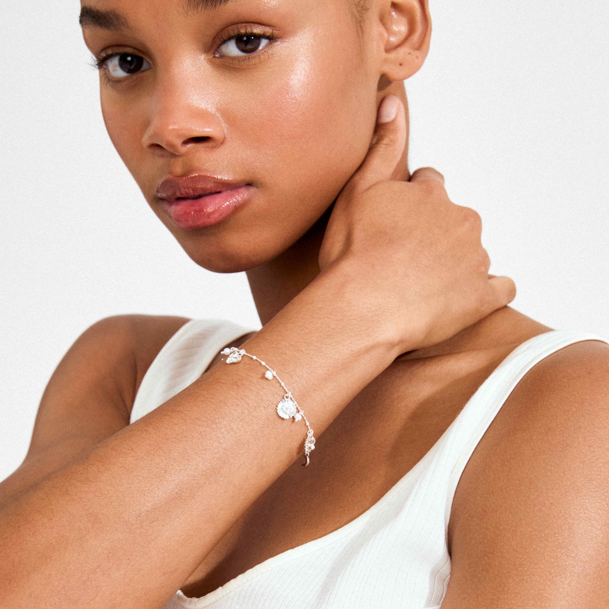 Bracelet fin argenté à breloques et perles, porté sur le poignet