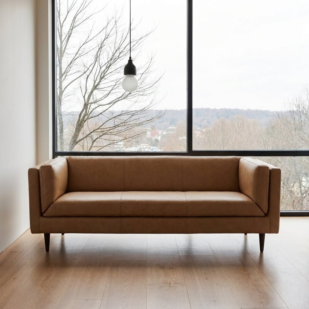 Canapé en cuir tan, dossier bas, coutures décoratives, accoudoirs épais, pieds fins