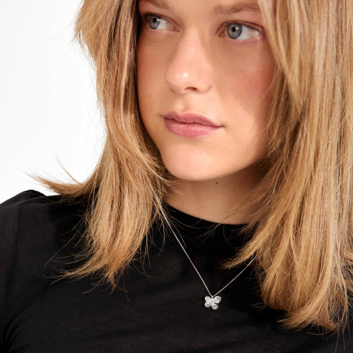 Collier plaqué argent et pendentif fleur, porté sur un haut noir