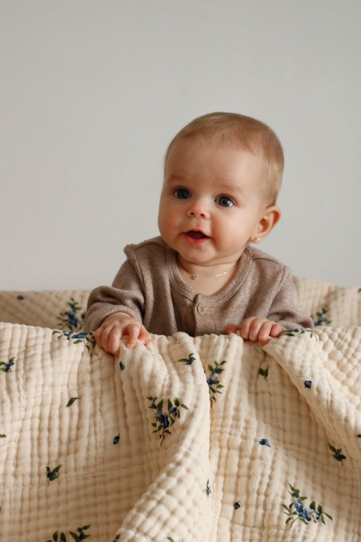 Couverture bébé en mousseline blanche à motifs fleuris bleu et vert, bébé la tient