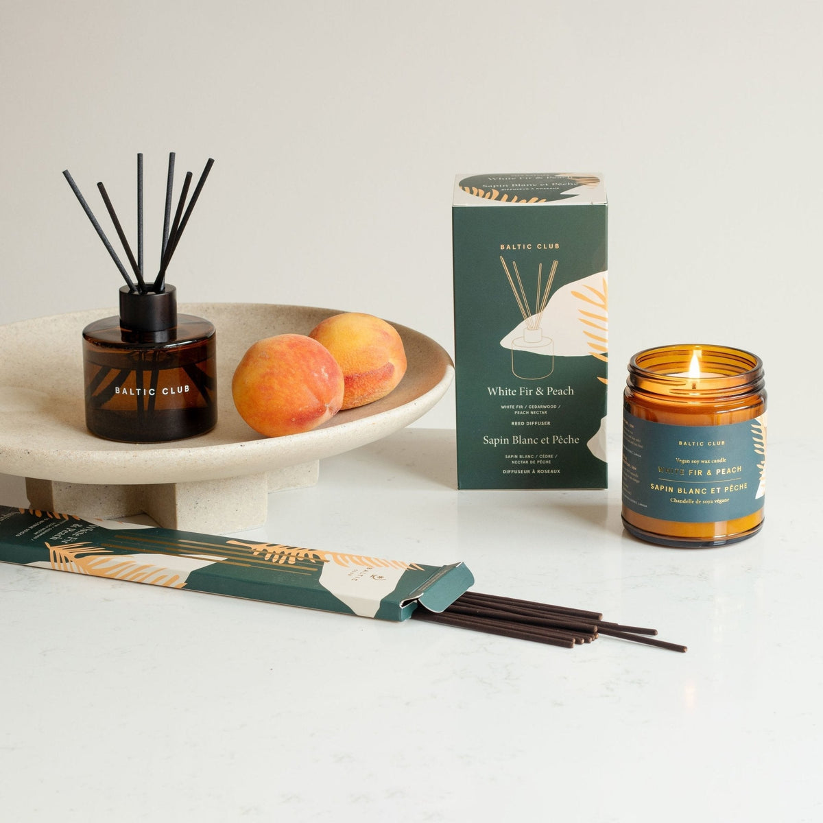 Diffuseur à roseaux flacon ambré, tiges noires, coffret et bougie parfumée allumée.