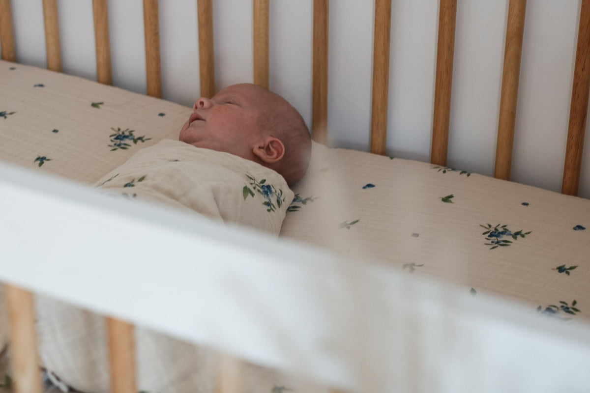 Drap contour en mousseline écrue avec motif fleuri bleu et vert, bébé endormi