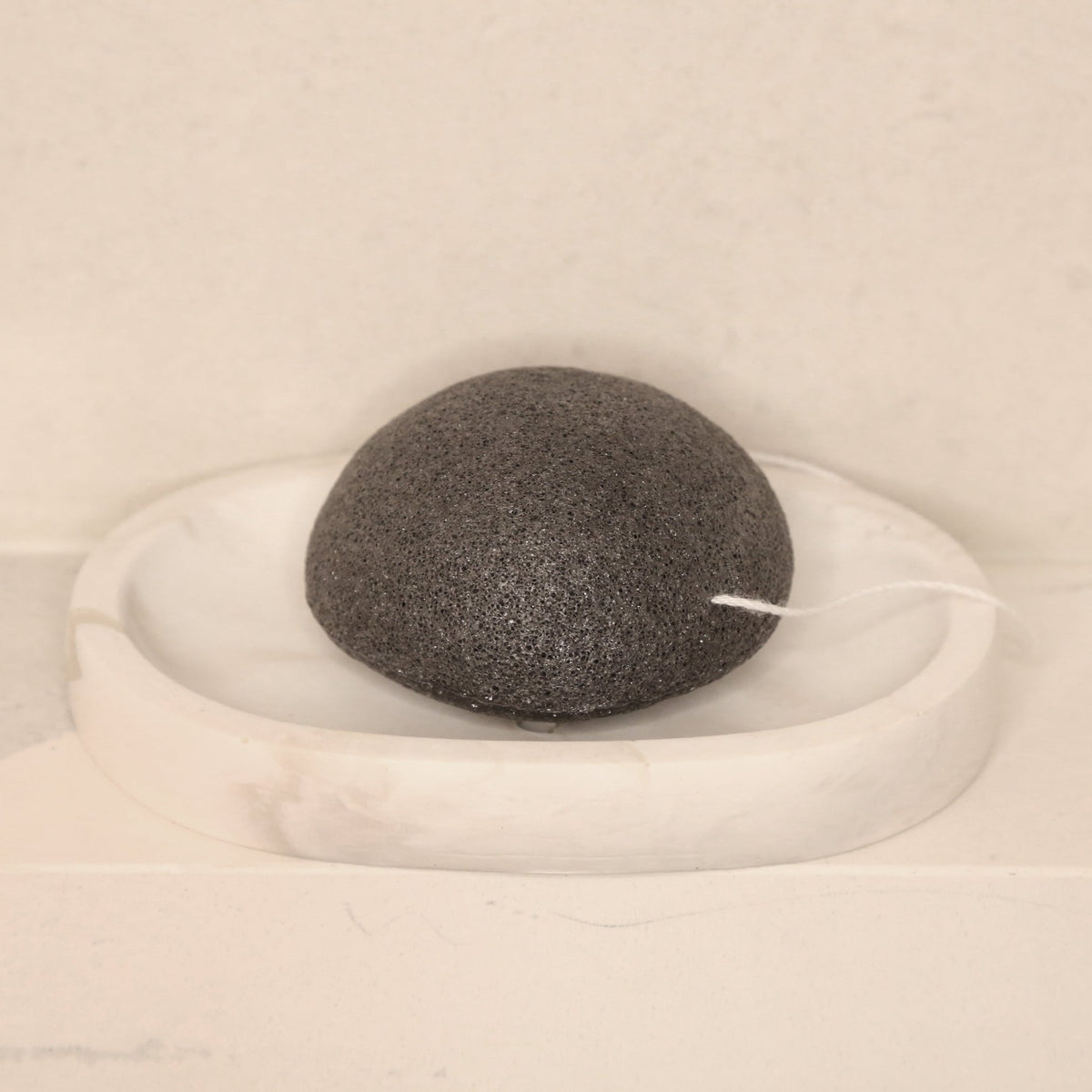 Éponge visage konjac ronde noire au charbon, posée sur un support blanc
