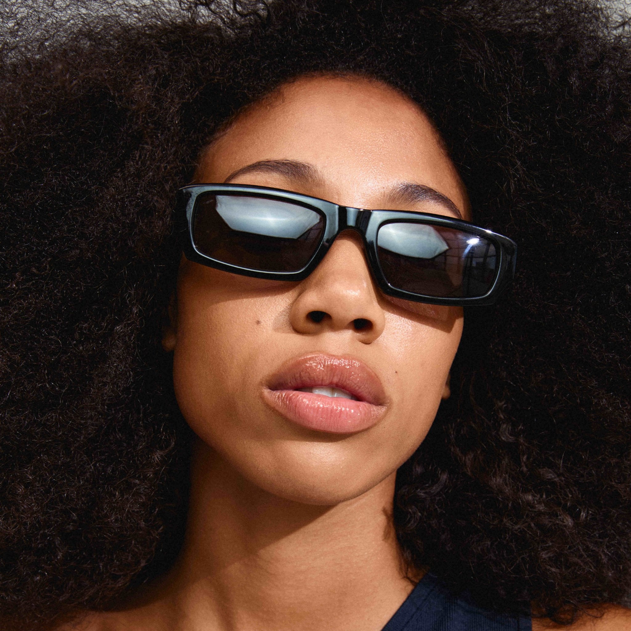 Lunettes de soleil noires, monture carrée, reflets sur les verres teintés.