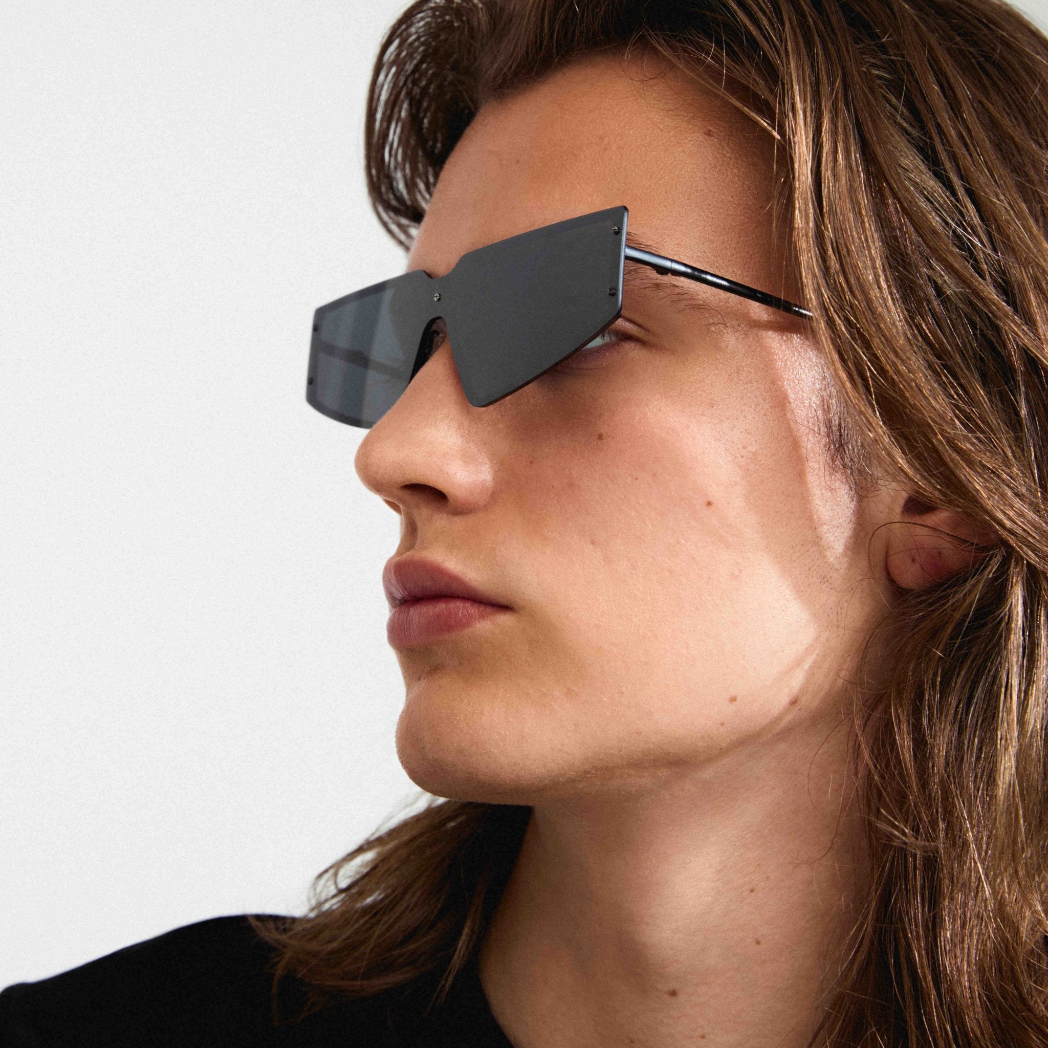 Lunettes de soleil noires en vue de profil, monture angulaire et branches fines.