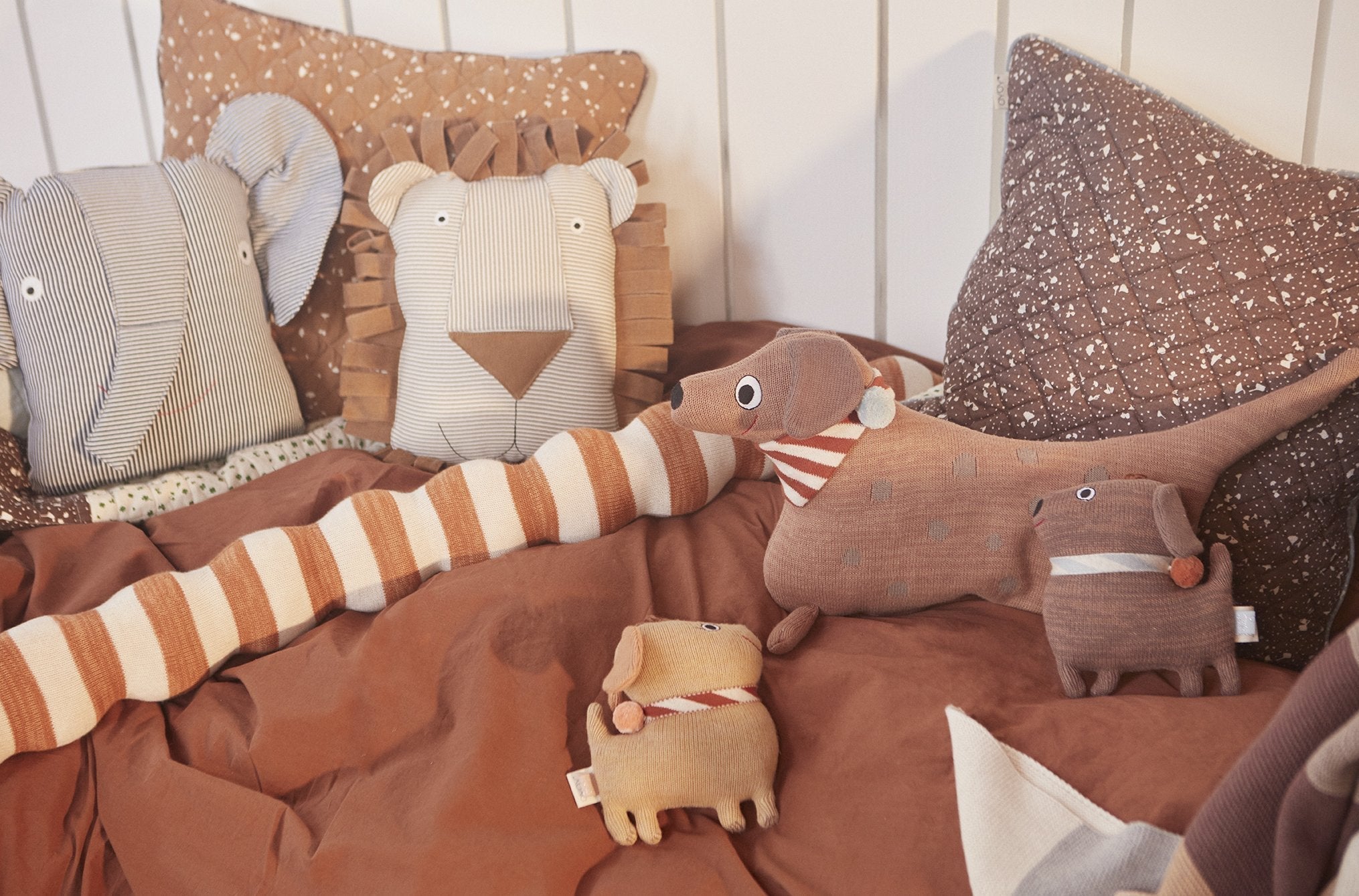 Lot de 3 peluches motif animal, rayures rouges et détails brodés, sur canapé.