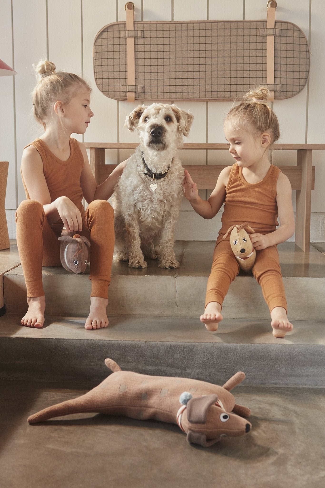 Peluche chien en tissu beige, yeux et museau brodés, avec petit accessoire rayé.