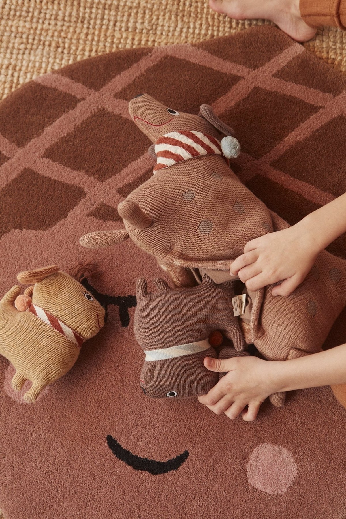 Trois peluches chien en coton tricoté, rayures rouges et museaux brodés, sur tapis.
