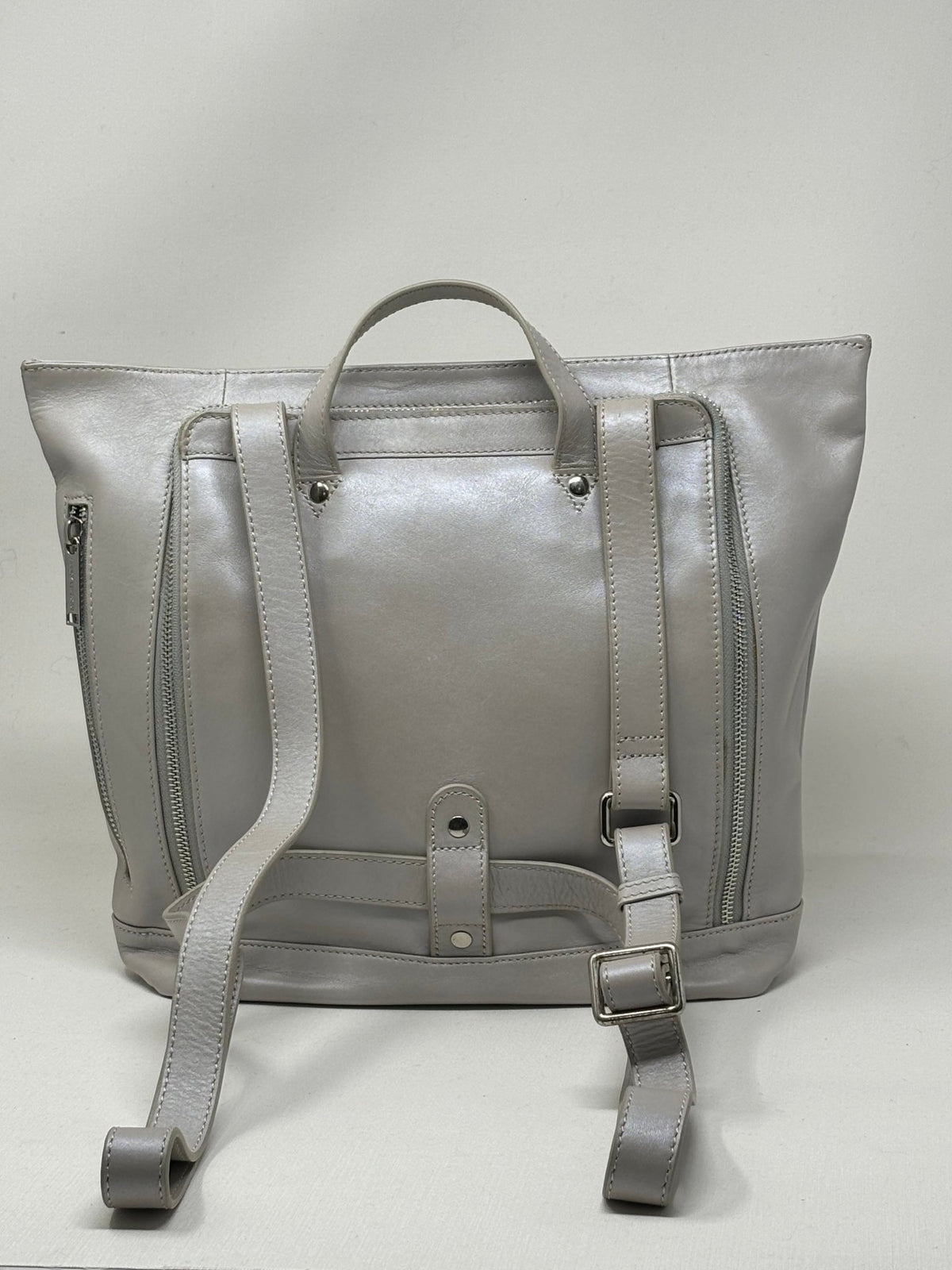 Sac à dos en cuir argent, vue arrière avec bretelles, poche zippée et patte centrale.
