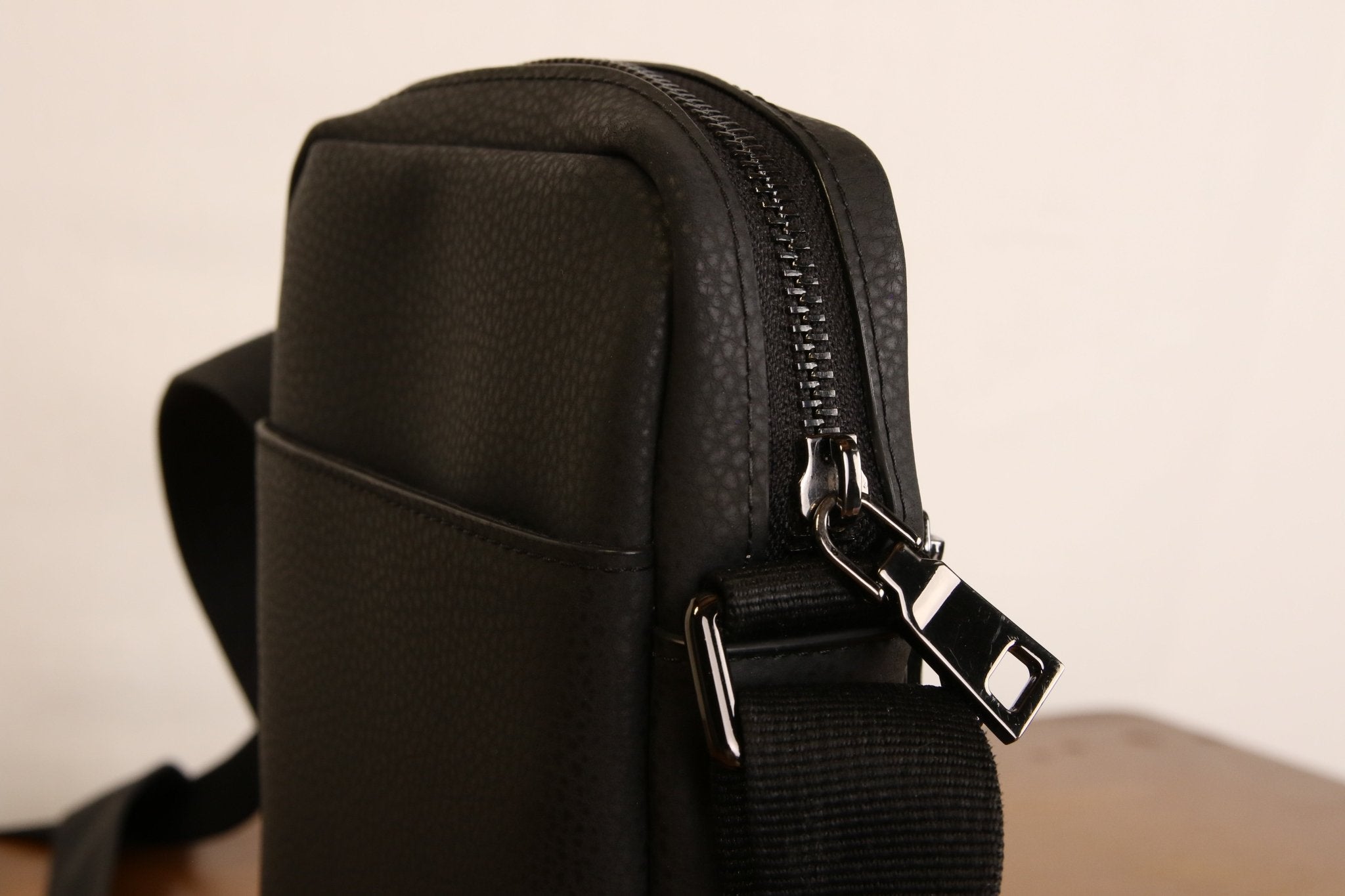 Sac bandoulière noir en cuir végétal, côté avec attache métallique et fermeture zippée