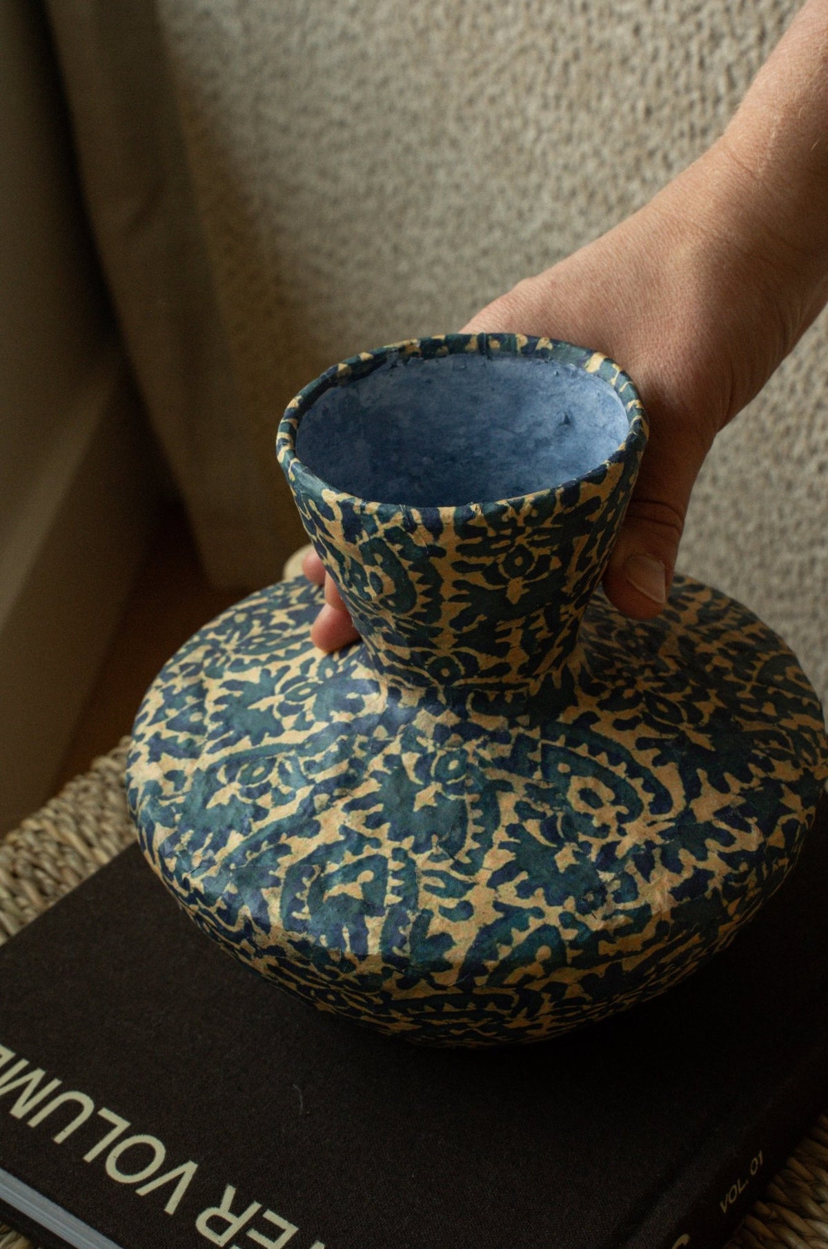 Vase trompette en papier mâché bleu foncé à motifs dorés, tenu en main.