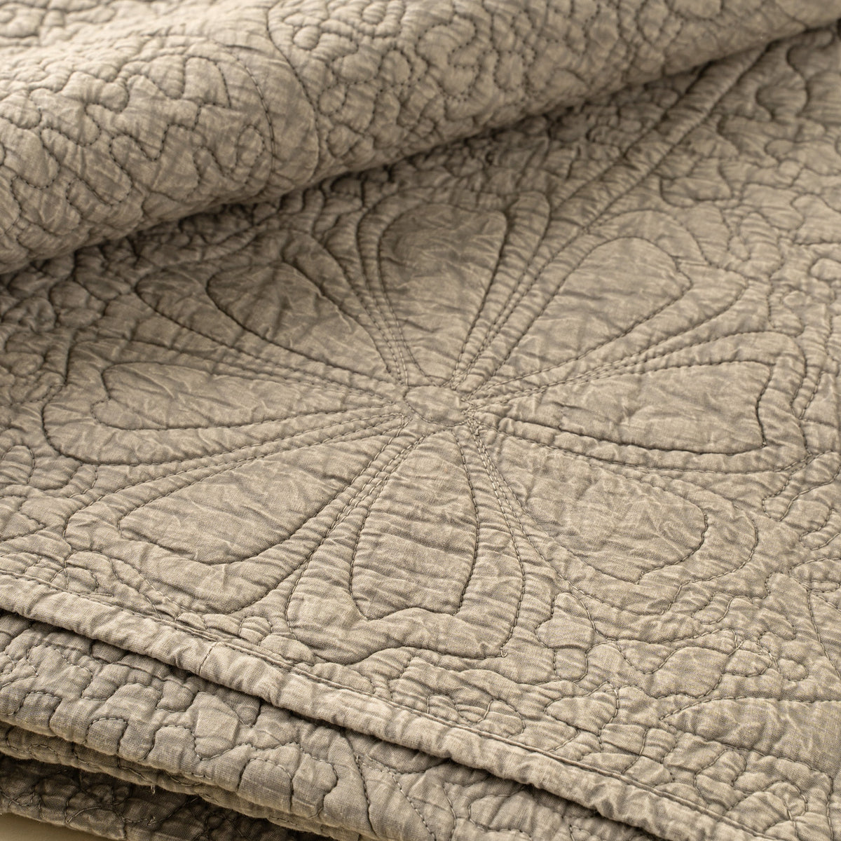 Couverture matelassée beige pierre, points apparents et relief du quilting, bord ourlé.