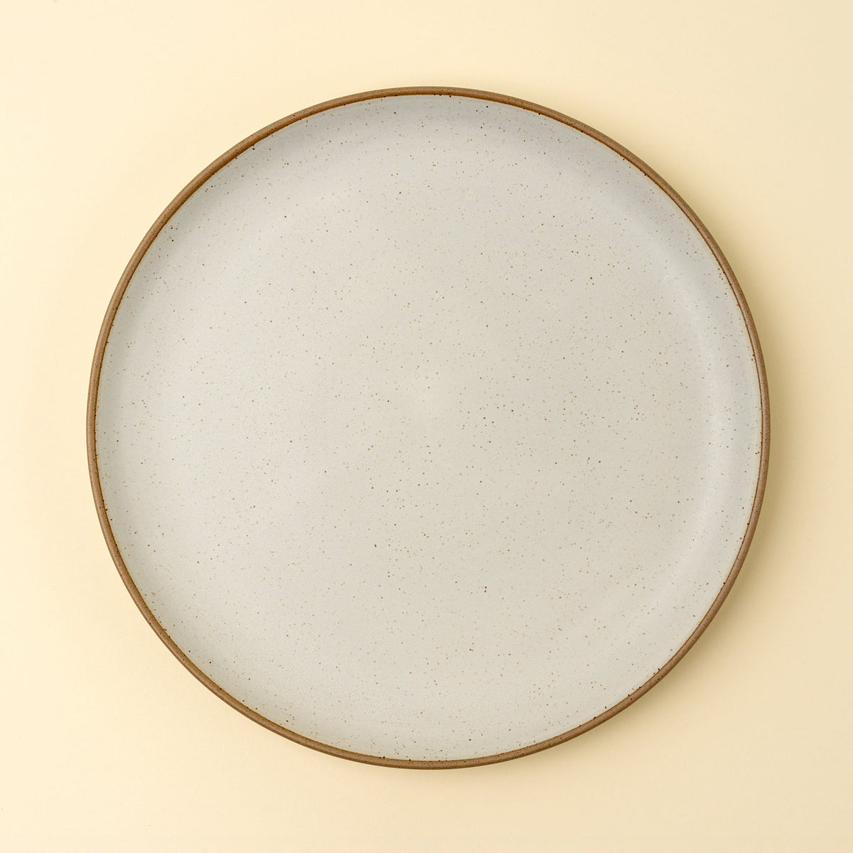 Assiette de présentation en grès ivoire, bord brun, décor moucheté, vue de dessus