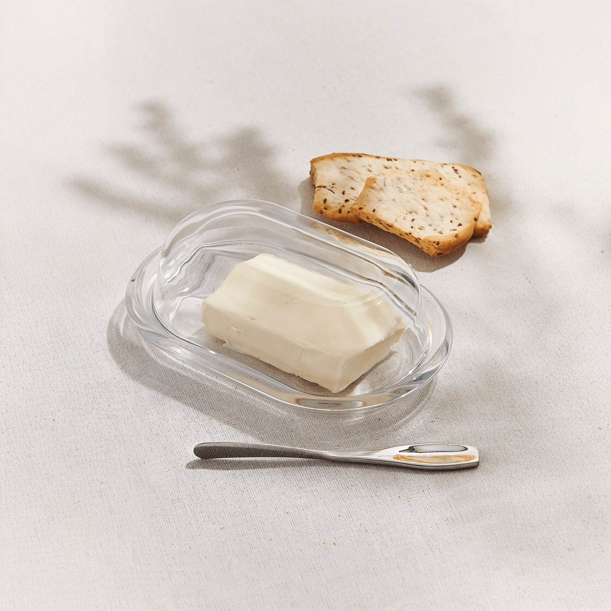 Beurrier en verre ouvert avec beurre, tranche de pain et couteau