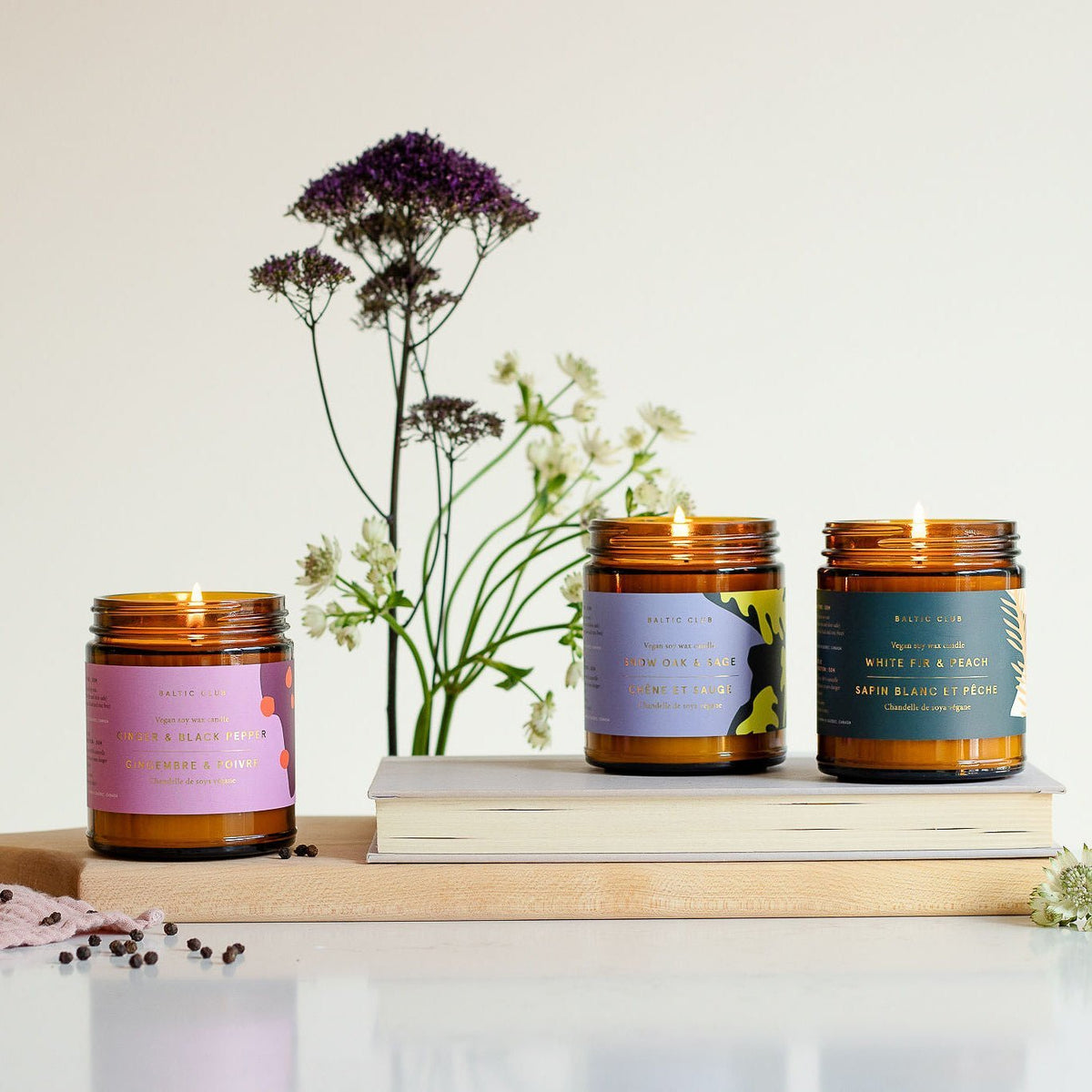Lot de trois bougies en pots ambrés, étiquettes violettes et vertes.