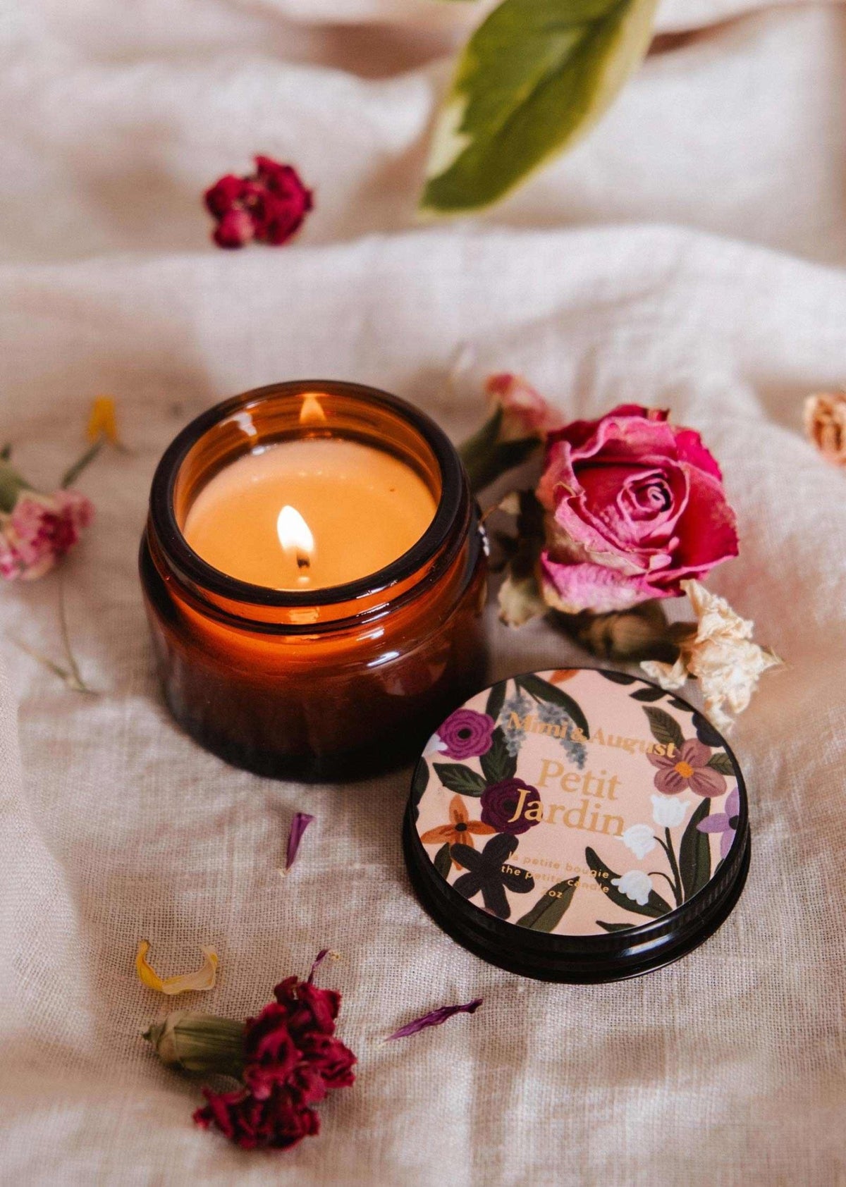 Bougie en pot en verre ambré, mèche allumée, couvercle noir à motif floral.