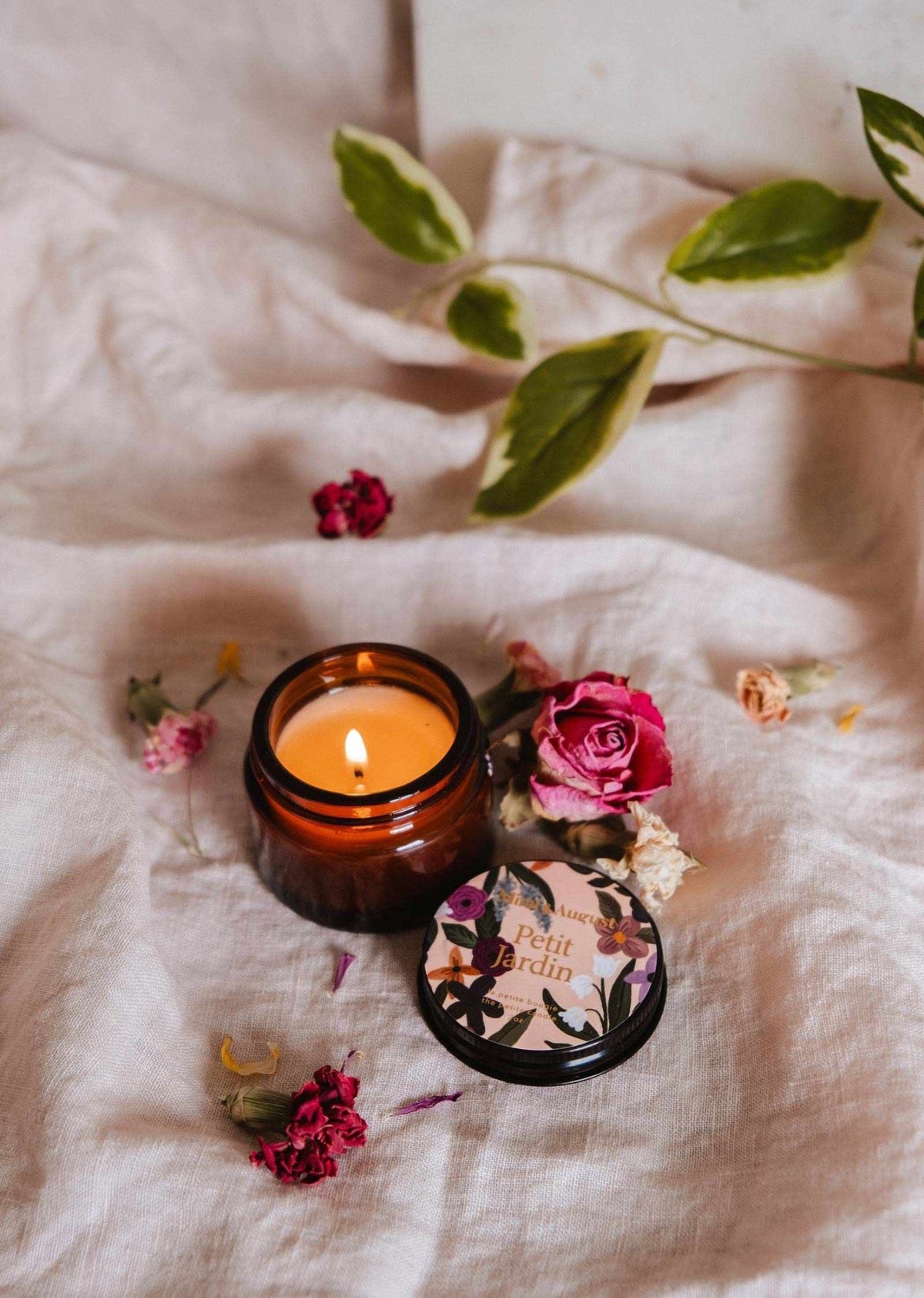 Bougie réutilisable en pot ambré, mèche allumée, couvercle noir floral.