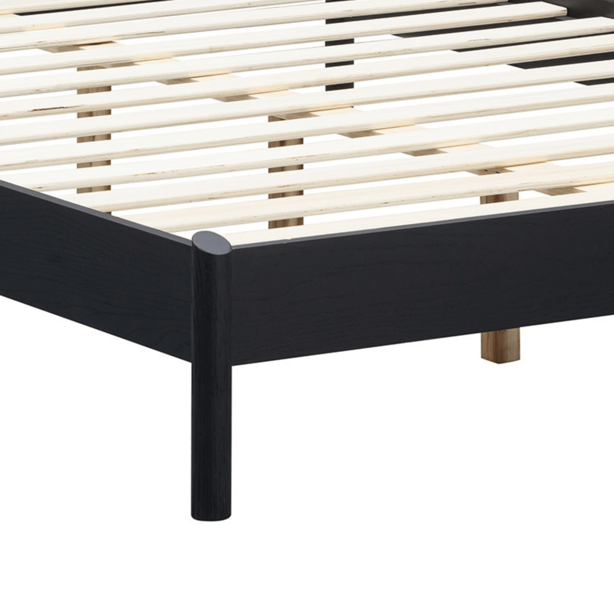 Détail du cadre de lit Gem noir avec pieds en bois clair et lattes blanches du sommier
