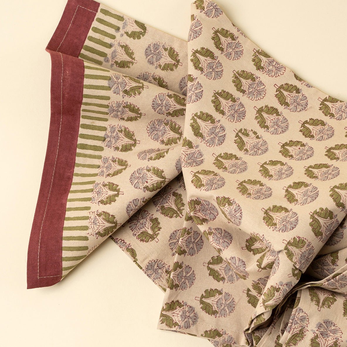 Chemin de table coton beige à motifs imprimés vert et mauve, bord bordeaux, vue pliée.