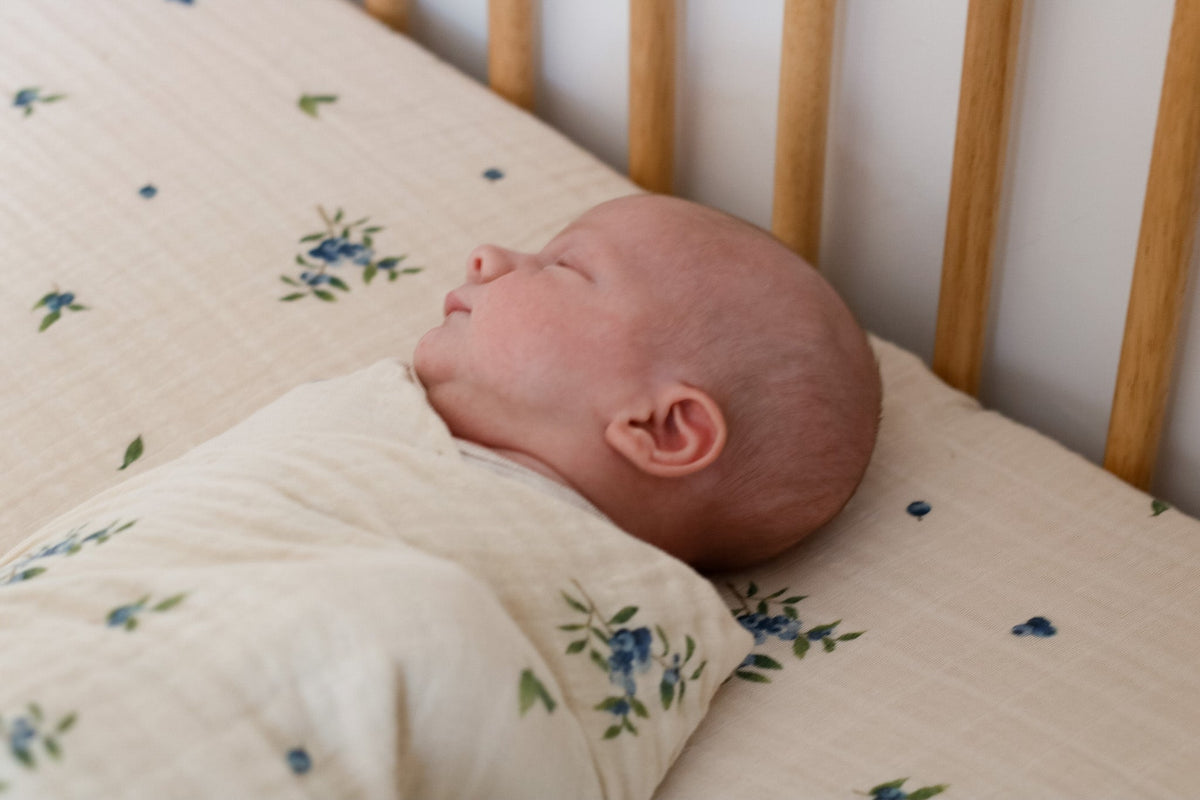 Bébé emmailloté dans une couverture en mousseline fond clair, fleurs bleues
