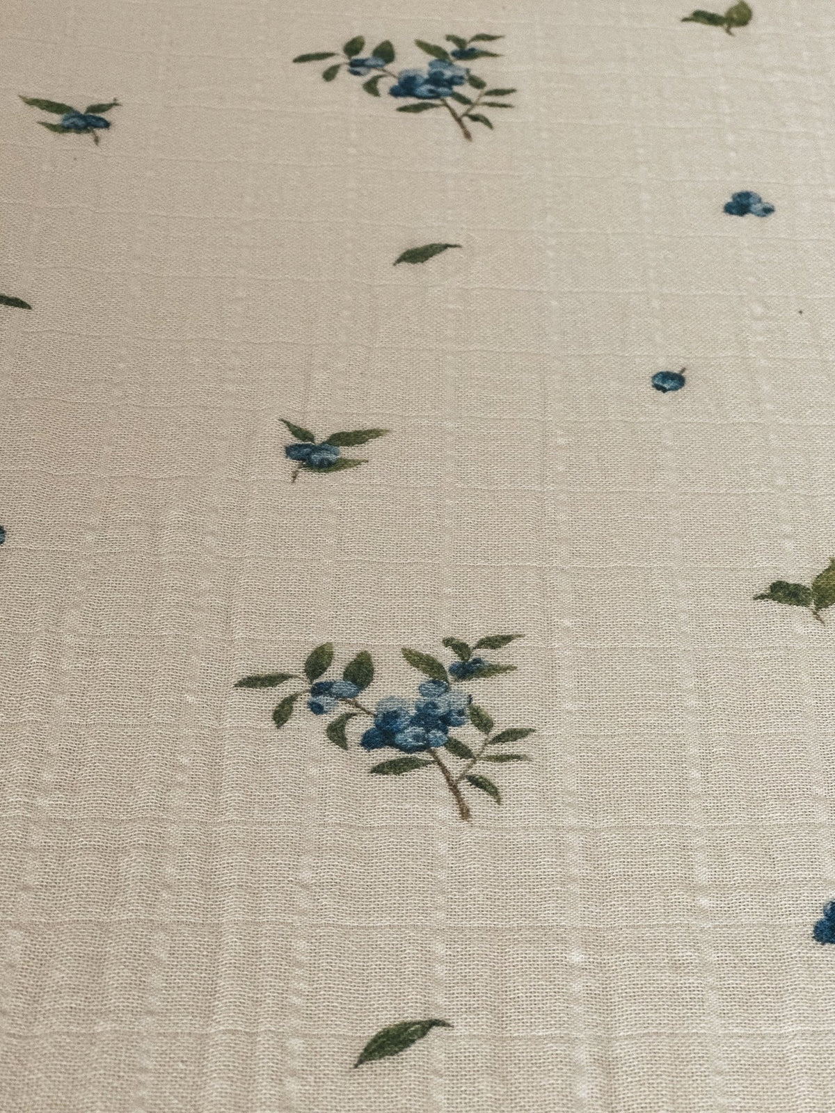 Détail de mousseline écrue : petites fleurs bleu et vert, texture finement gaufrée
