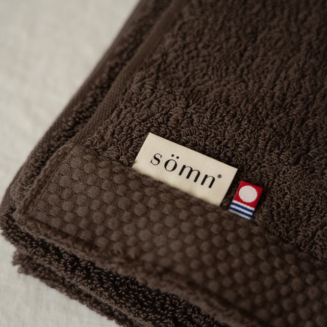 Serviette en coton brun foncé, bord texturé et étiquette sömn