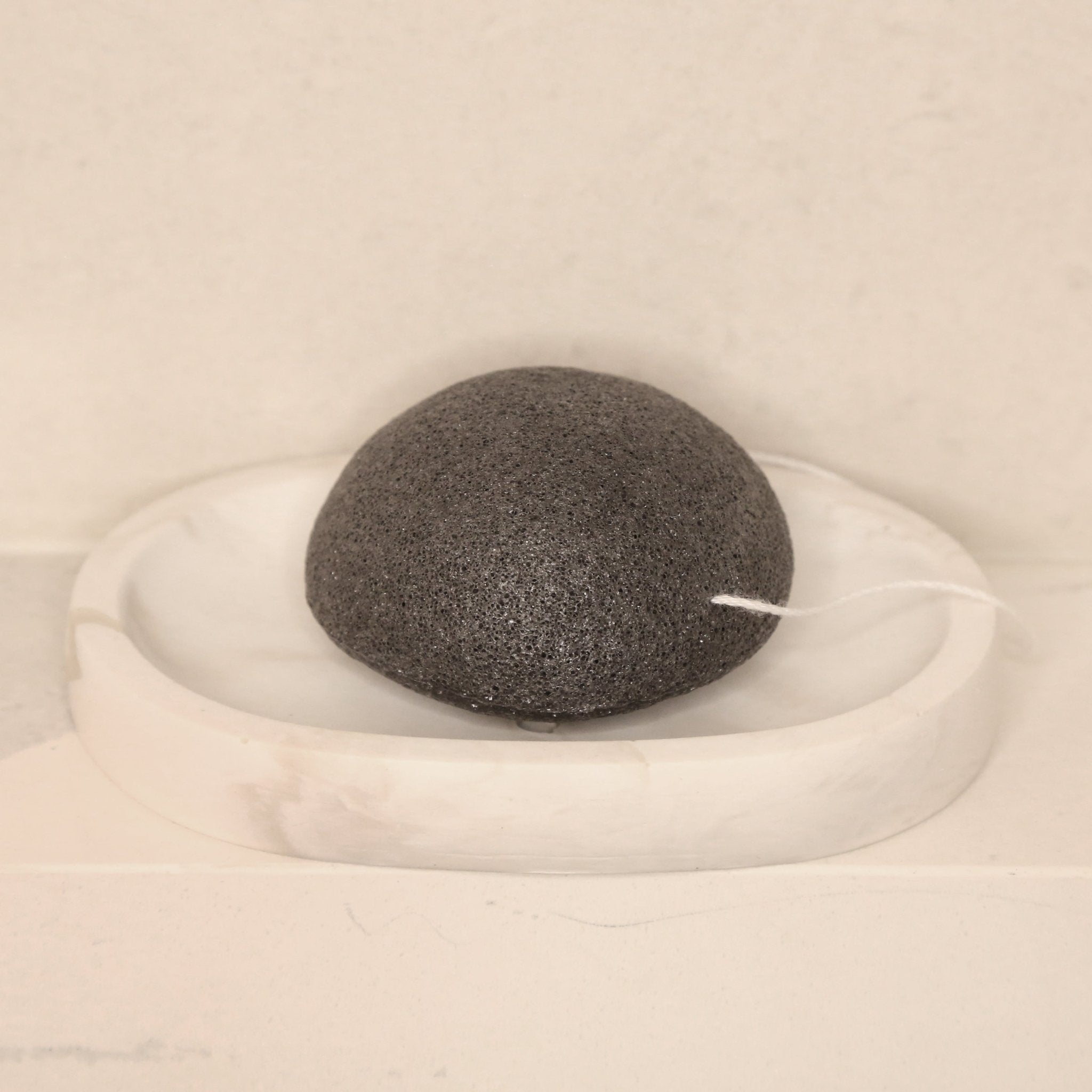 Éponge visage konjac ronde noire au charbon, posée sur un support blanc