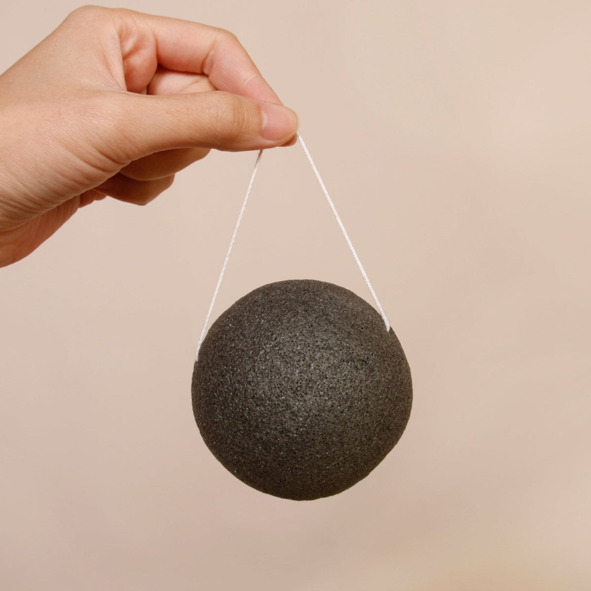 Éponge visage konjac ronde noire au charbon, tenue par une main avec ficelle