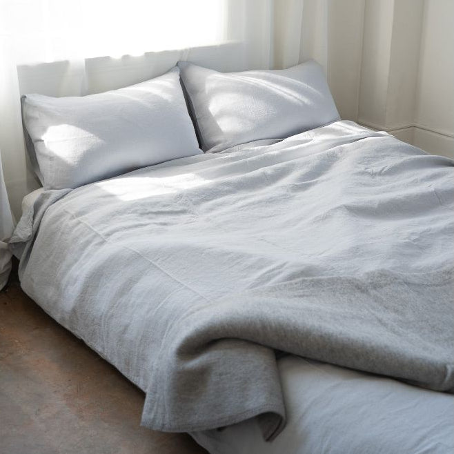 Jeté en laine gris clair sur lit, drapé sur une couette et deux taies