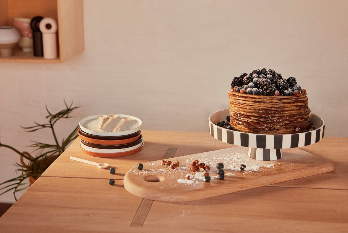 Plateau décoratif en céramique à rayures noir et blanc, avec gâteau et bord annelé.