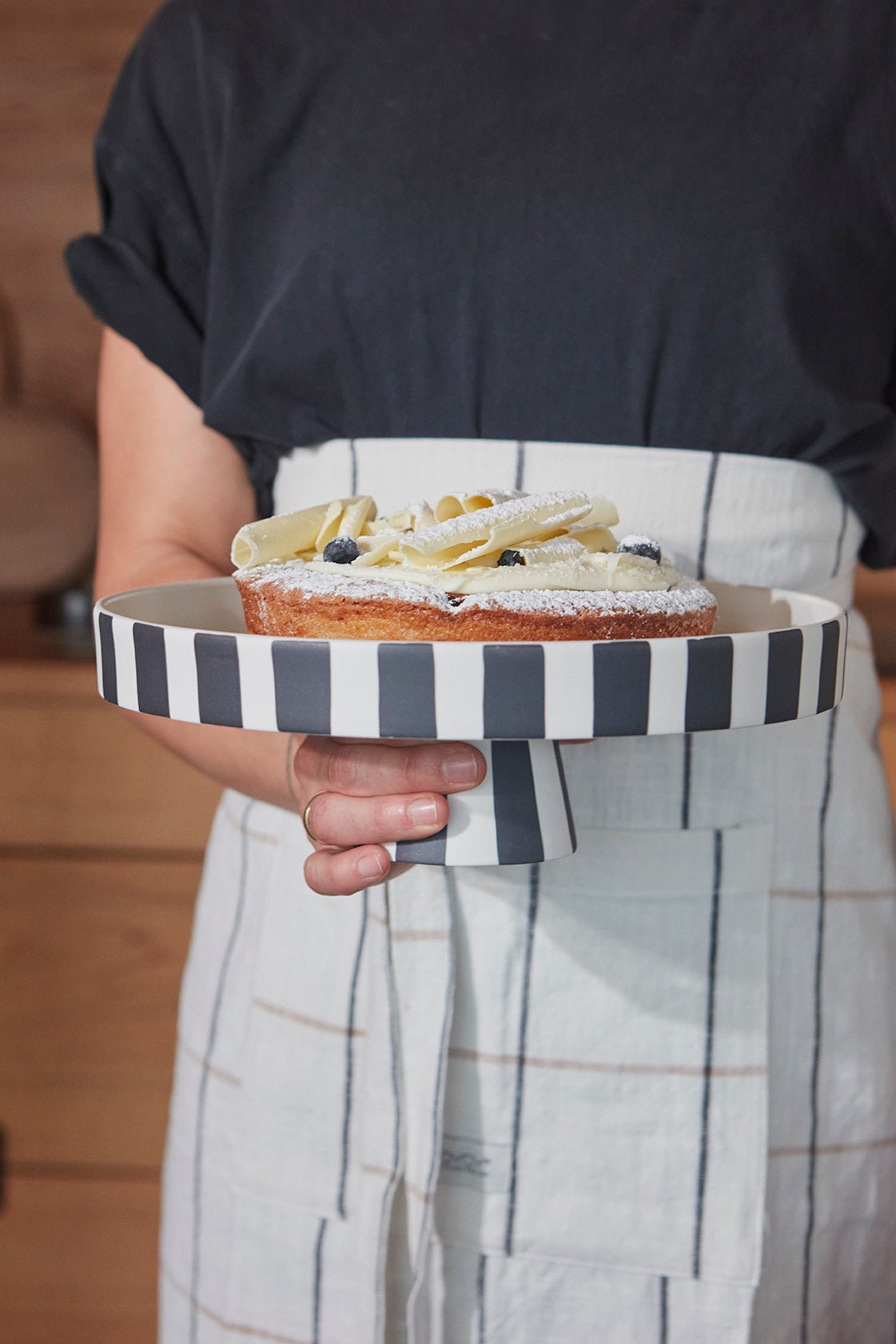 Plateau décoratif en céramique à rayures noir et blanc, tenu à la main, avec gâteau.