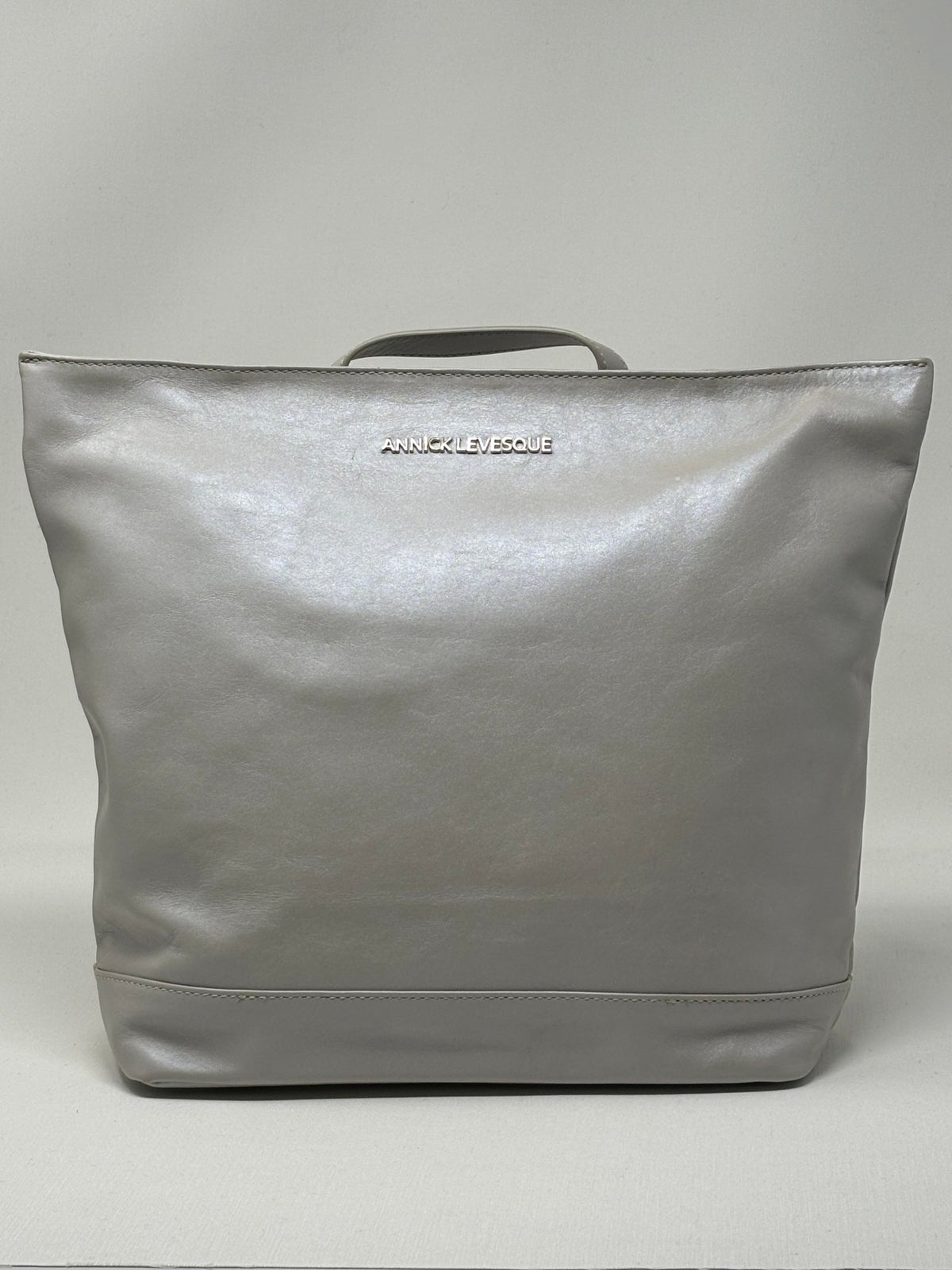 Sac à dos en cuir argent, face arrière lisse avec logo discret en haut.
