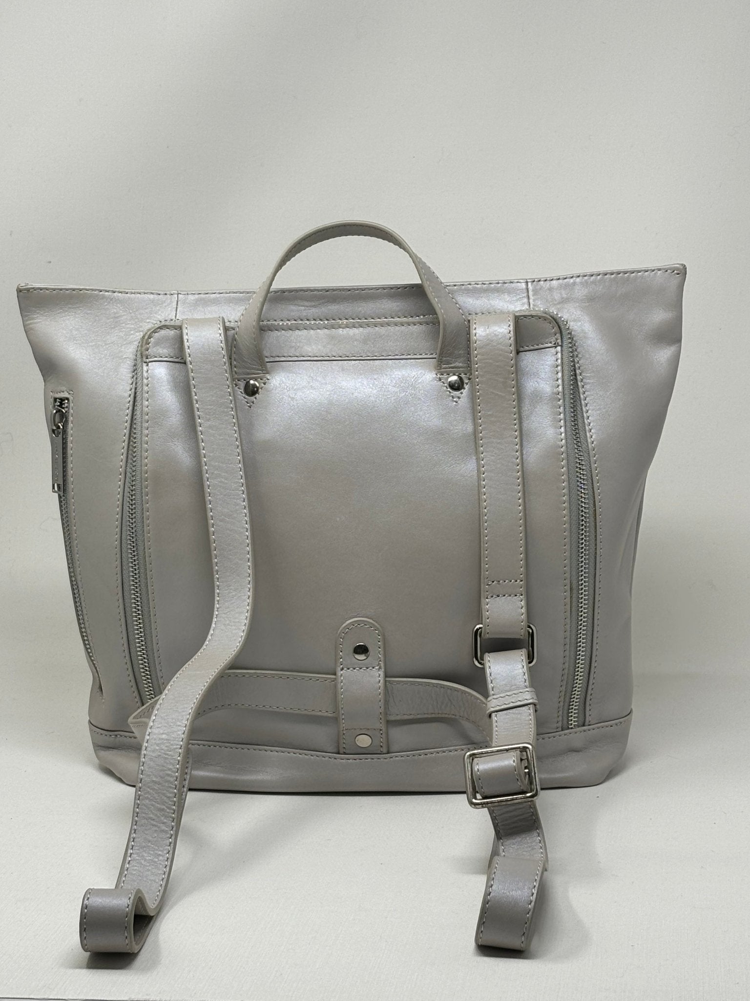 Sac à dos en cuir argent, vue arrière avec bretelles, poche zippée et patte centrale.
