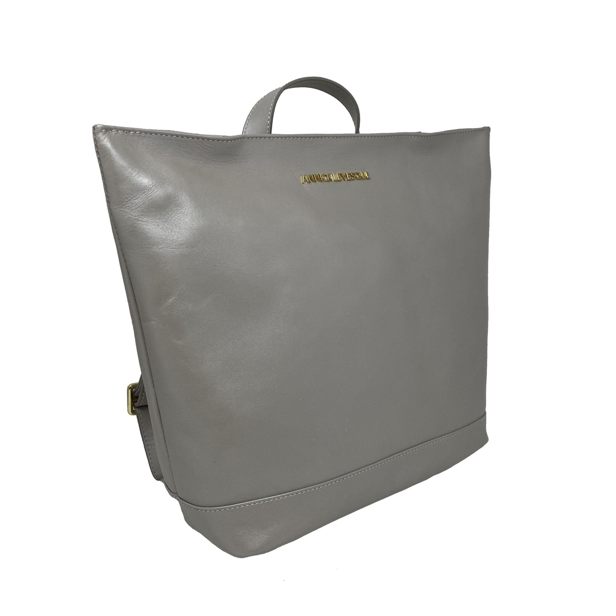Sac à dos en cuir argent trapèze, anses et fermeture éclair latérale visible.