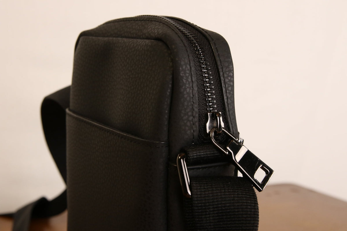 Sac bandoulière noir en cuir végétal, côté avec attache métallique et fermeture zippée
