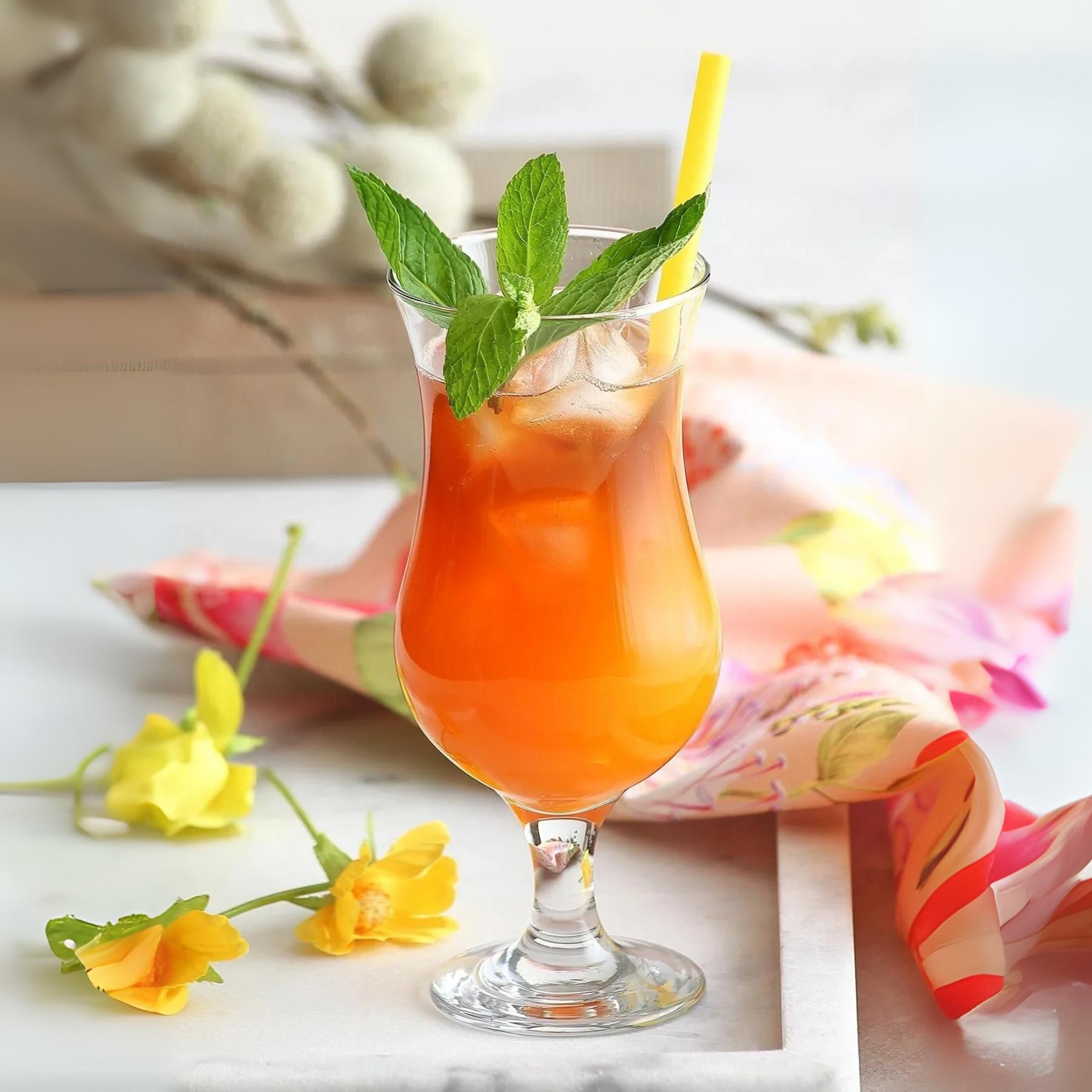 Verre à cocktail hurricane en verre transparent, pied et cannelures, boisson orange.