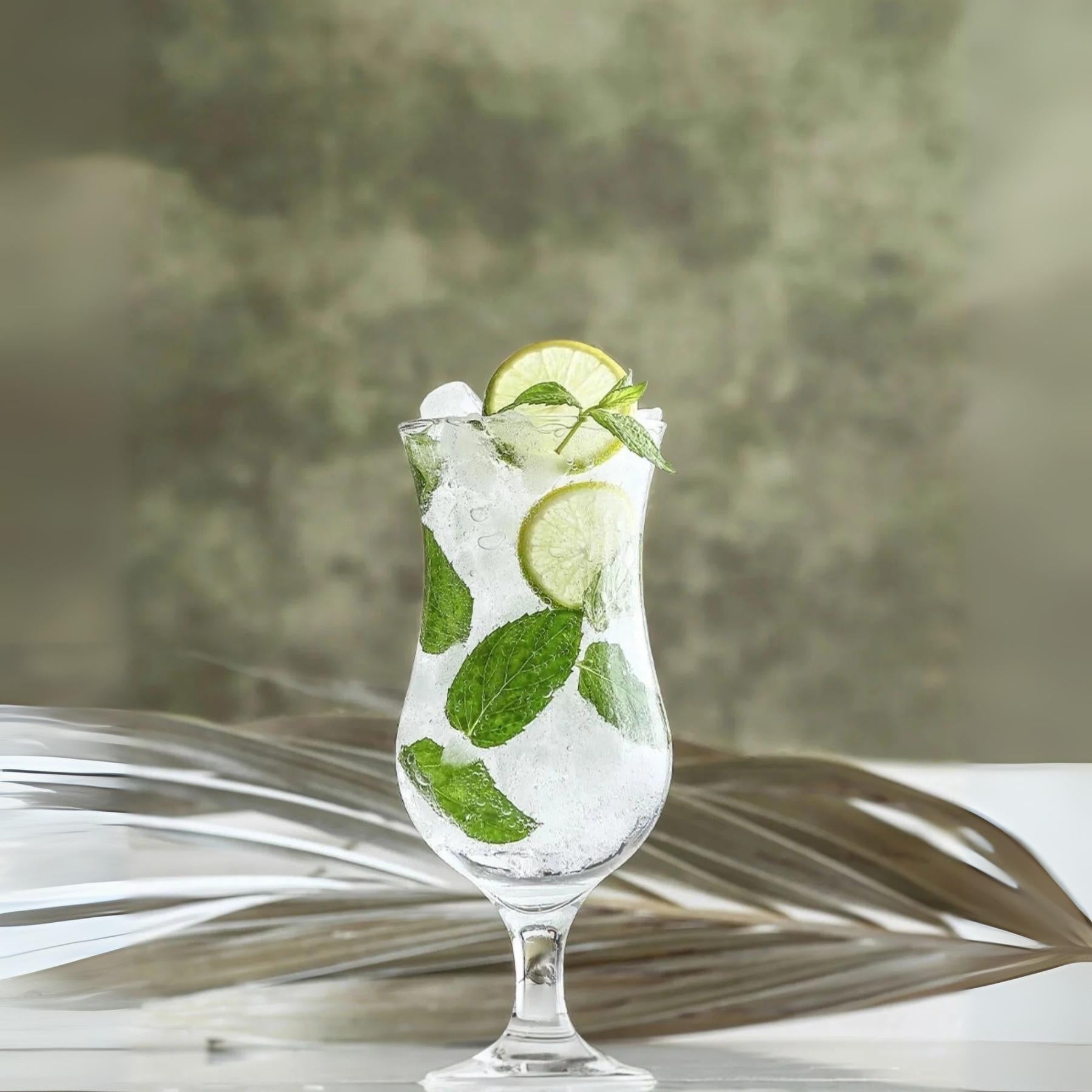 Verre à cocktail hurricane transparent rempli de glaçons, menthe et rondelles vertes.