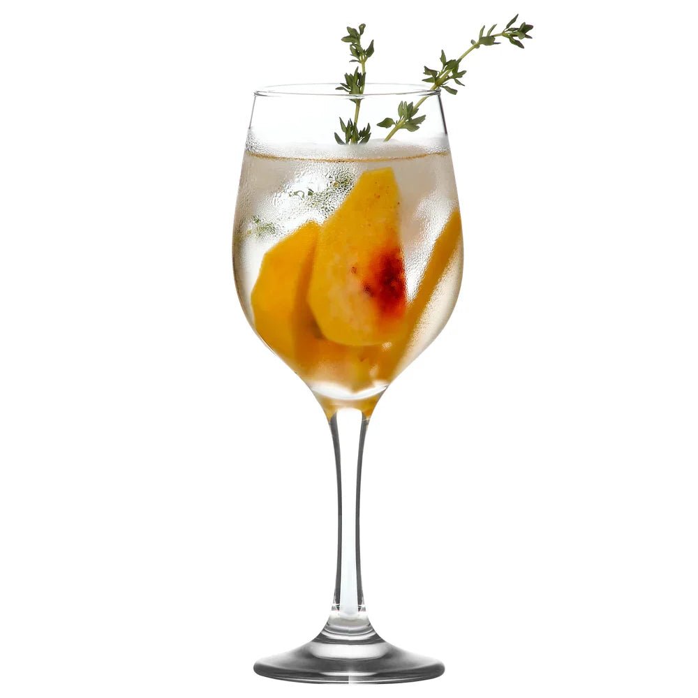 Verre à vin transparent à pied gravé, rempli de boisson avec morceaux de fruit.